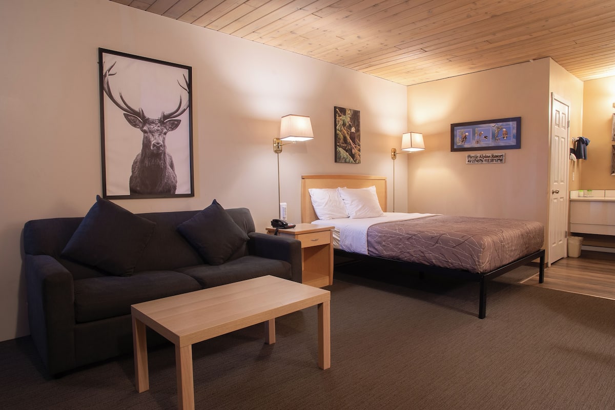 Una habitación de hotel con una cama, un sofá, una mesita de noche, una lámpara y un cuadro enmarcado con una cierva.