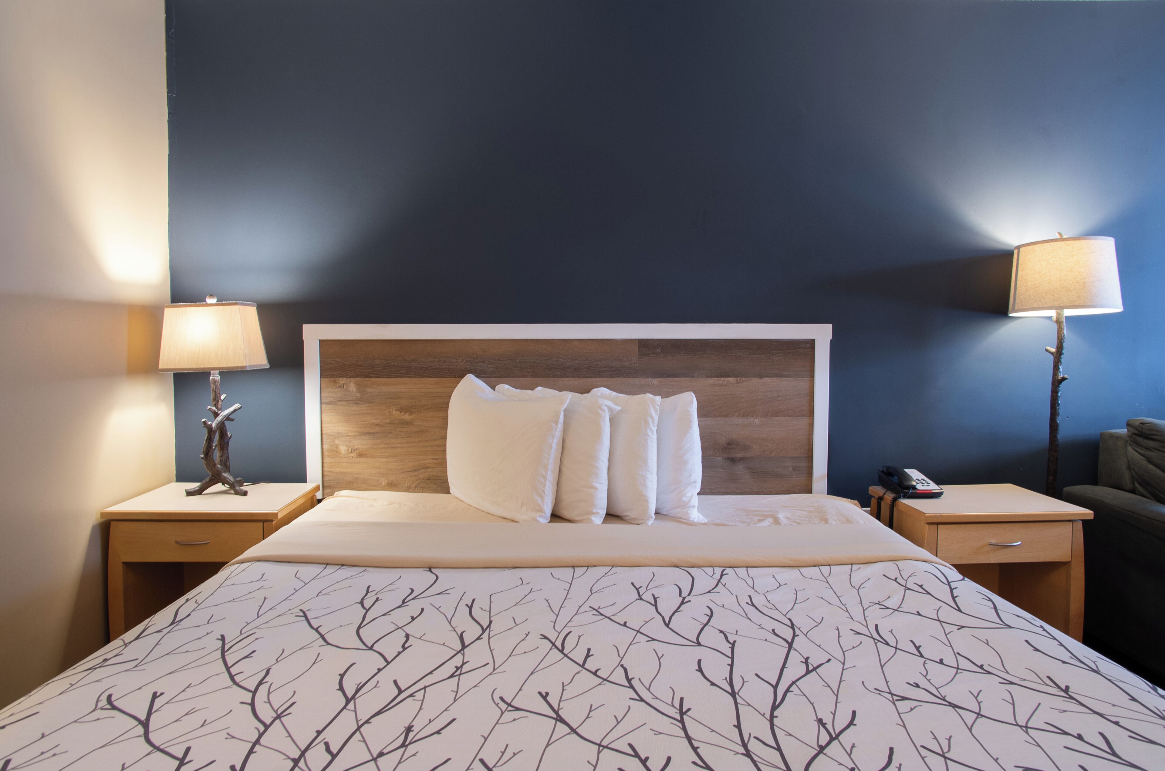 A hotel room with a large bed, two bedside tables with lamps, a wooden headboard, and a dark blue wall.