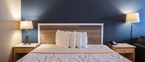 Habitació d'hotel amb un llit gran, dues taules de nit amb làmpades, un panell de capçalera de fusta i una paret blava fosca.