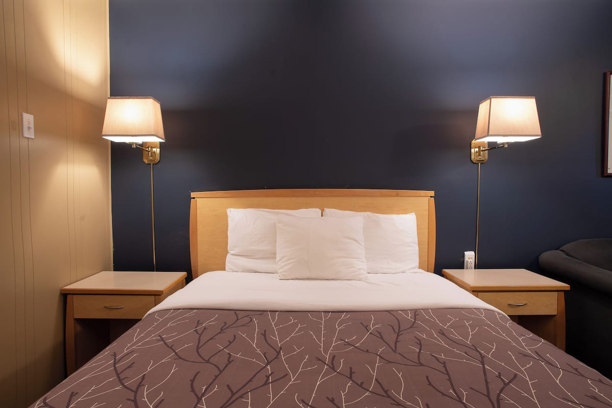 Una habitación de hotel con una cama grande, dos lámparas de noche, un cabecero de madera y una mesita de noche con cajón.
