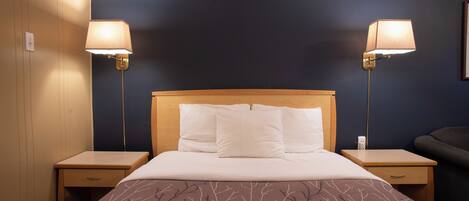 Een hotelkamer met een groot bed, twee bedlampen, een houten hoofdeinde en een nachtkastje met een lade.