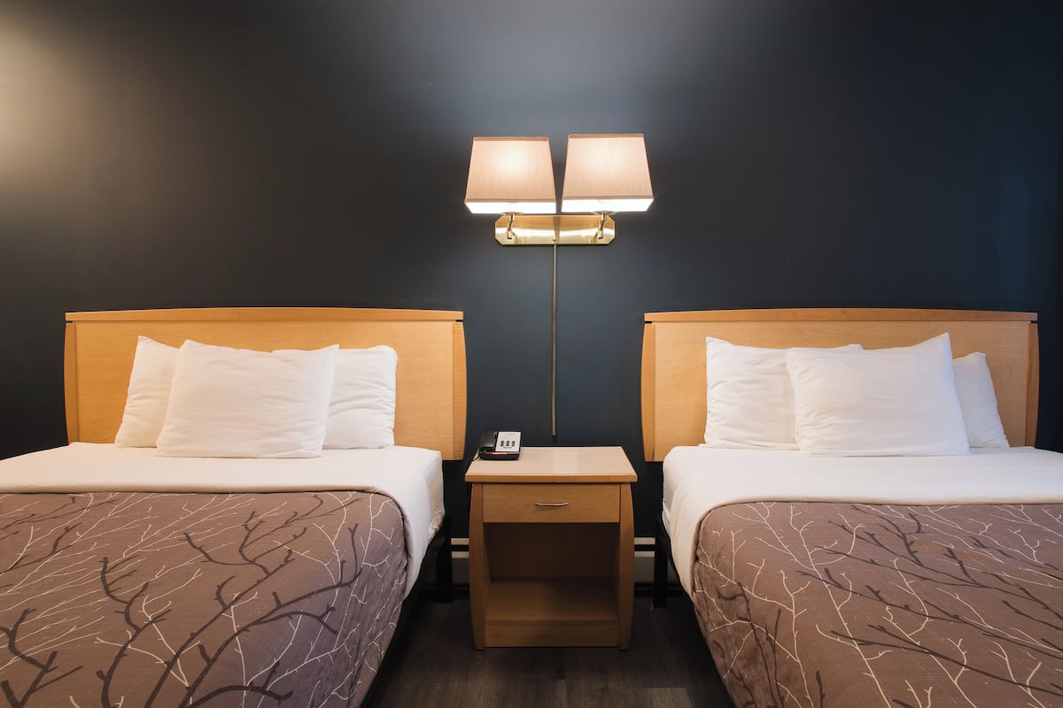 Habitación de hotel con dos camas, una mesita de noche con lámpara y un aplique de pared.