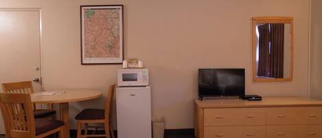 A room with a dining table and chairs, a microwave, a television on a dresser, a map on the wall, and a window with curtains.
