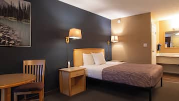 A hotel room with a bed, bedside tables, a chair, a desk, and a painting of a mountain landscape.