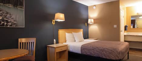 Una habitación de hotel con cama, mesitas de noche, una silla, un escritorio y un cuadro de un paisaje montañoso.