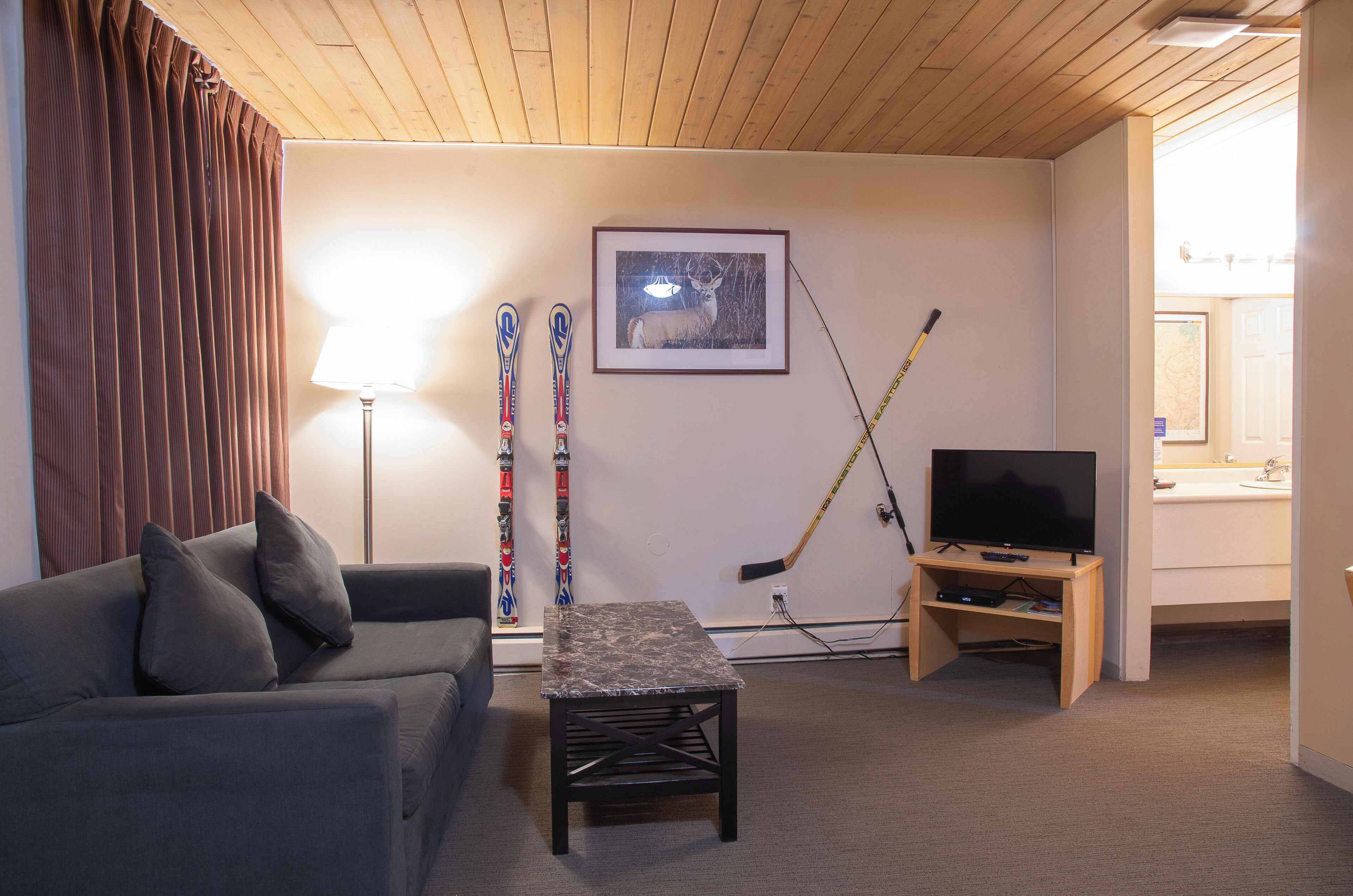 A living room with a sofa, a table, a TV, skis, and a hockey stick.