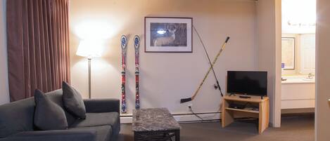A living room with a sofa, a table, a TV, skis, and a hockey stick.