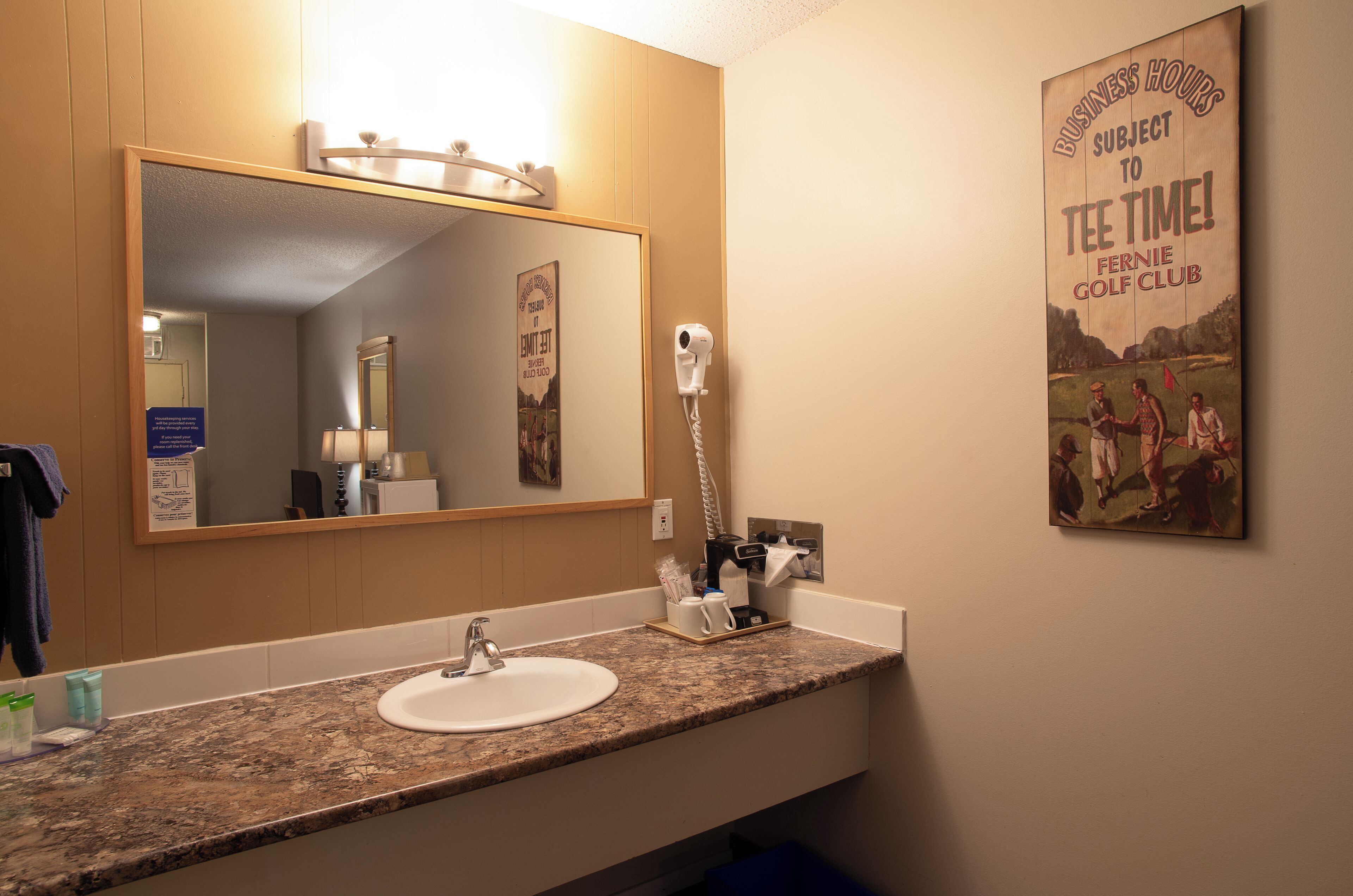 Une salle de bain avec un lavabo, un miroir et une affiche faisant la promotion des heures de départ au club de golf Fennie.