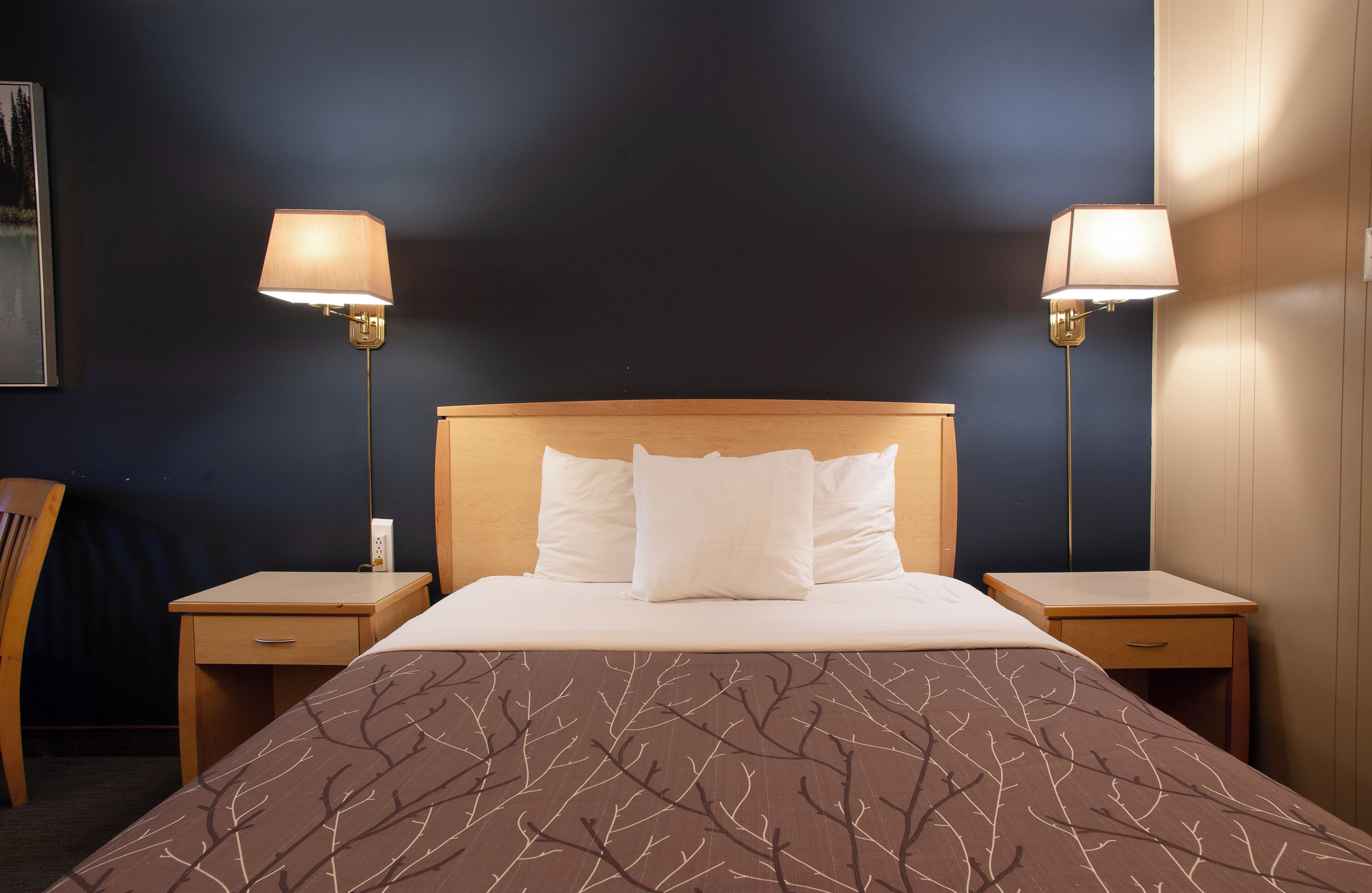 Una habitación de hotel con una cama grande, dos mesitas de noche y dos lámparas fijadas a la pared.