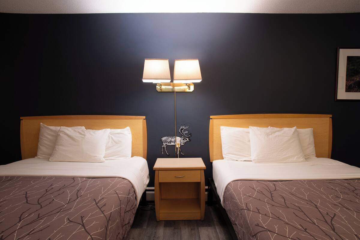 Una habitación de hotel con dos camas, una mesita de noche, una lámpara y un cuadro colgado en la pared.