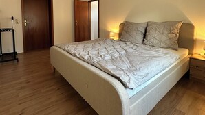 A bedroom with a bed, wooden flooring, a door, and a nightstand with a lamp. - FAMILY-FRIENDLY VACATION APARTMENT IN THE CENTER OF BRAUNLAGE (Braunlage)