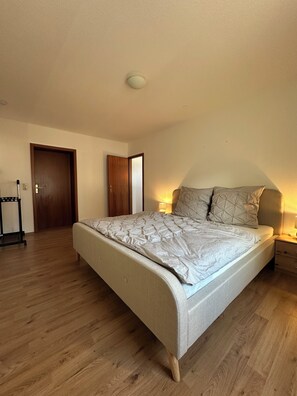 Ein Schlafzimmer mit einem Bett, Holzboden, einer Tür und einem Nachttisch mit Lampe.