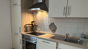 A compact kitchen with white cabinets, a stove, a sink, and a range hood. - FAMILY-FRIENDLY VACATION APARTMENT IN THE CENTER OF BRAUNLAGE (Braunlage)