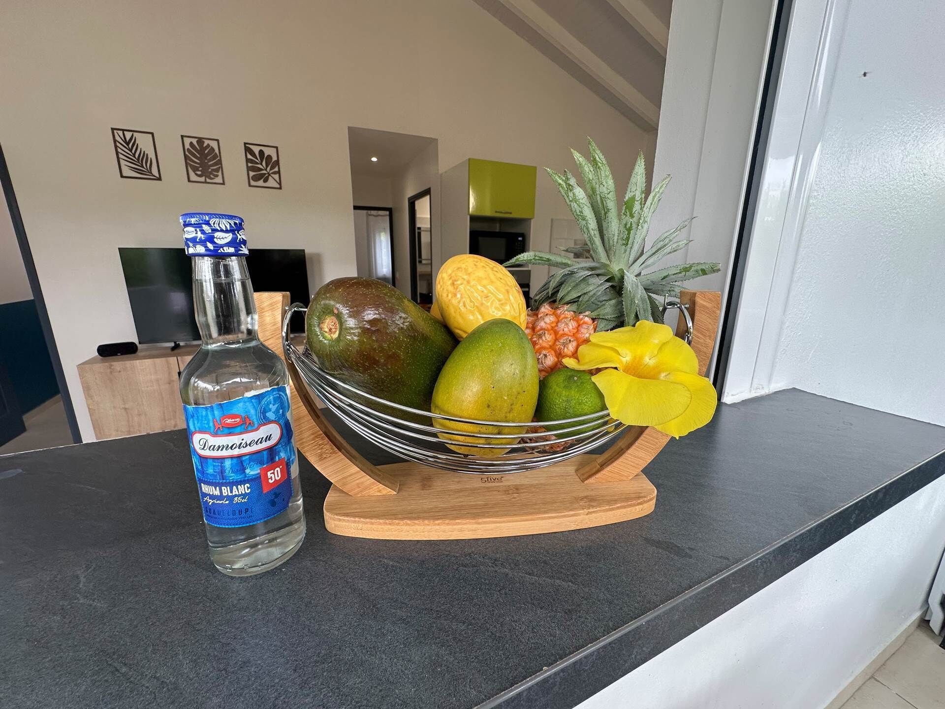 Eine Küchenarbeitsplatte mit einer Rumflasche, einer Obstschale voller Früchte und einem Fernseher im Hintergrund.