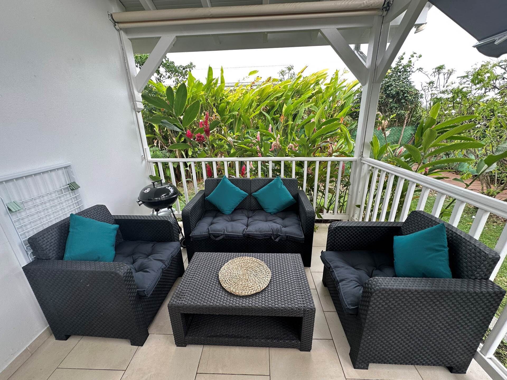 A covered outdoor seating area with wicker furniture and a grill.