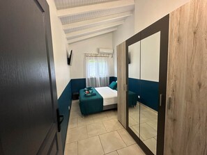 Ein Schlafzimmer mit einem Bett, einem Spiegel, einem Fenster mit Vorhängen und einer Tür.