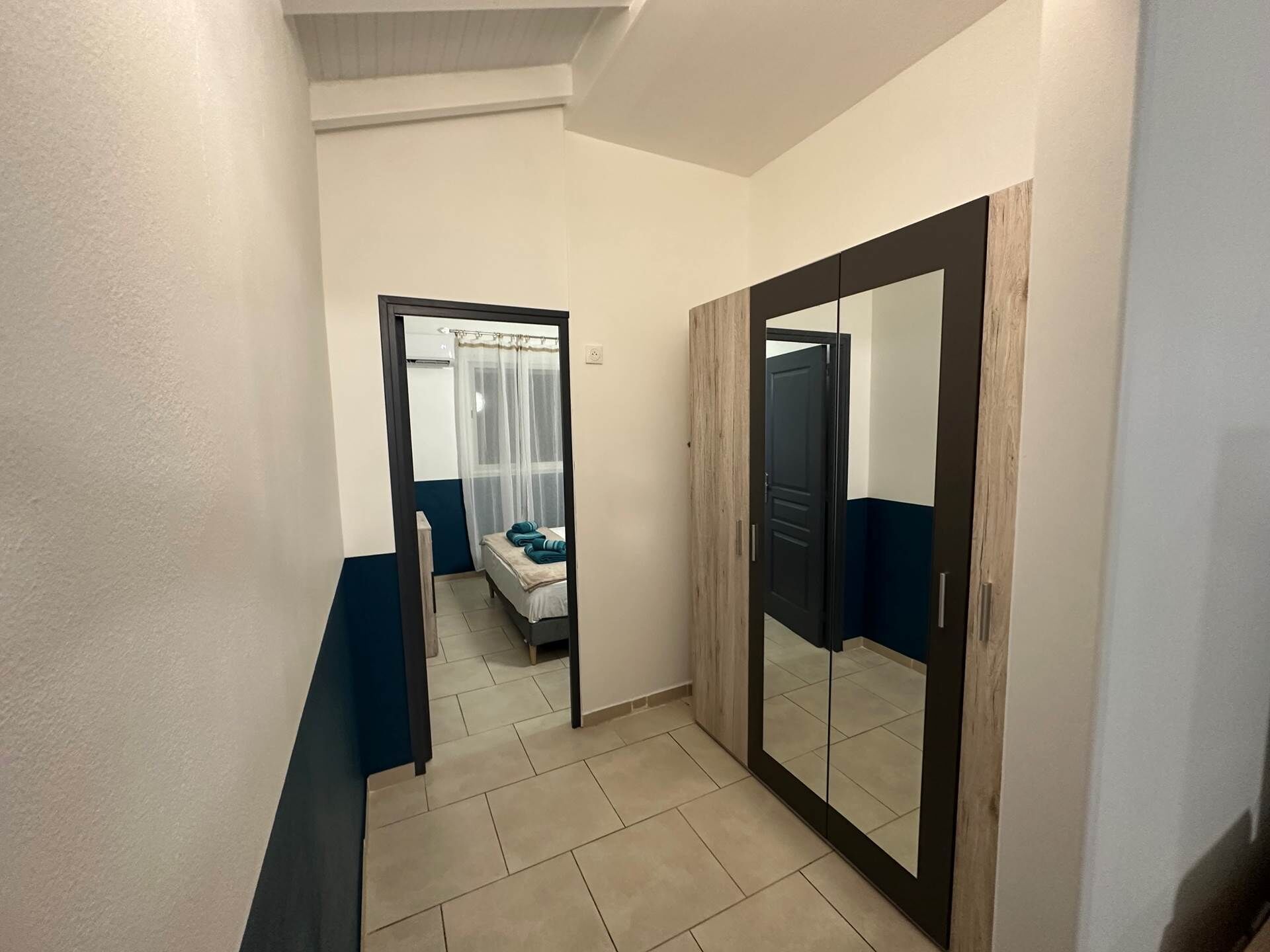 Un couloir avec un lit, un miroir et une porte donnant sur une autre pièce.