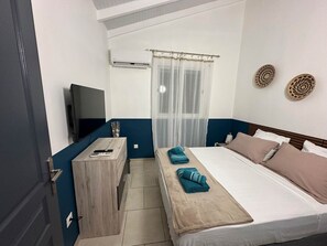 Hotellihuone, jossa on sänky, työpöytä, televisio ja ilmastointilaite.