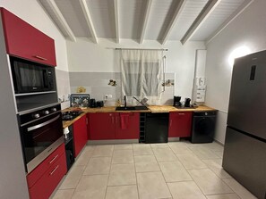 Eine kleine Küche mit roten Schränken, einer Mikrowelle, einem Herd, einem Spülbecken und einem Kühlschrank.