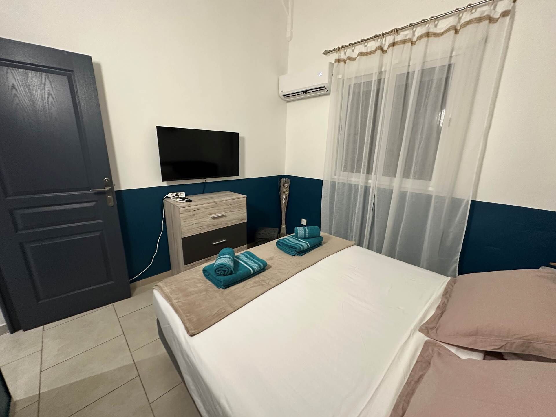 A hotel room with a bed, a TV, a dresser, and a window with curtains.