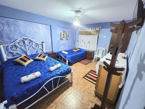 Une chambre avec deux lits, une armoire en bois, un ventilateur de plafond et une fenêtre avec des rideaux.