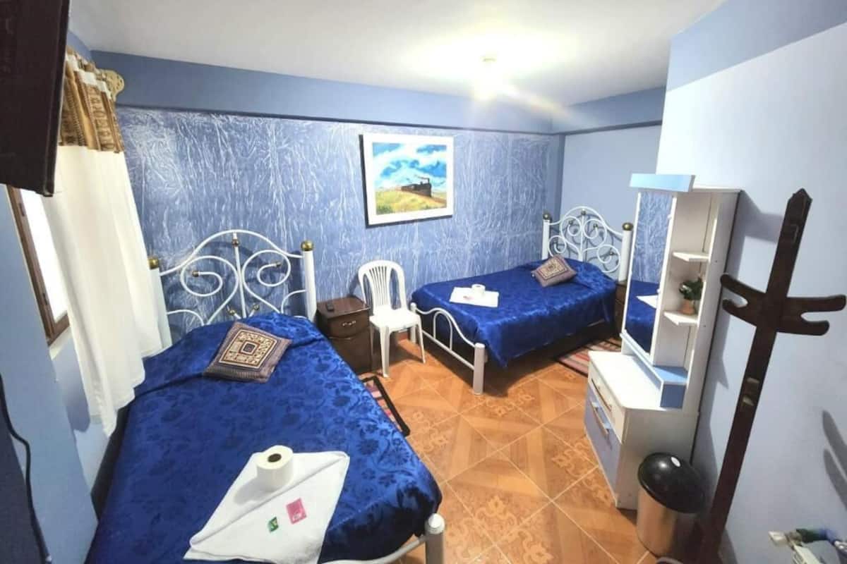 A bedroom with two beds, a chair, a desk, and a mirror.