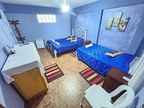 A room with two beds, a small table, a chair, a radiator, and a window. - Hotel Aguilar (Uyuni)