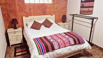 Una cama con un colorido edredón a rayas, dos almohadas decorativas, una mesita de noche con una lámpara y un tendedero de pared.