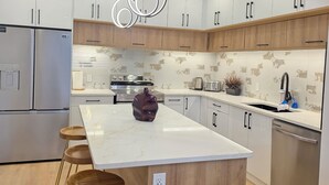 A modern kitchen with white cabinets, a marble island, wooden stools, and stainless steel appliances. - Pakallen De-Paris Ensuite Master Bdrm 5 min to UofA, UofA Hospital. Free wifi (Edmonton)