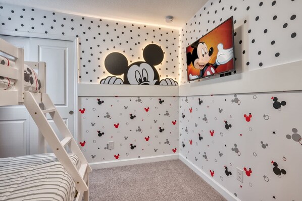 A child's room with Mickey Mouse wall decals, a bunk bed, and a TV mounted on the wall.