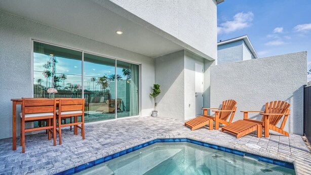 A modern outdoor pool area with a glass-enclosed patio, wooden chairs, and a small table. - Spacious villa with themed bedrooms and private pool (Kissimmee)