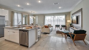 A modern kitchen with a central island, a dining area with a sofa and chairs, and a living room with a TV and seating. - Spacious villa with themed bedrooms and private pool (Kissimmee)