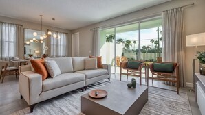 A modern living room with a sofa, coffee table, and chairs. There is a large window with a view of palm trees. - Spacious villa with themed bedrooms and private pool (Kissimmee)