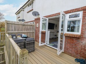 Een patio met een houten terras, een zithoek met kussens en een bakstenen muur.