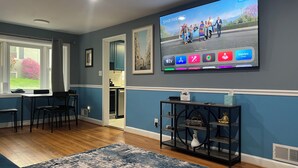 A living room with a flat-screen TV mounted on the wall, a dining area with chairs, a coffee table, and a rug. - Family friendly Home, 3BR, Old Town, Nat. Harbor & DC. Nice neighborhood (Alexandria)