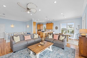 A spacious living room with a grey sectional sofa, a wooden coffee table, and a kitchen in the background. - Blue Palms- 4/3 Gulf View home, WIFI, great views! (Cape San Blas)