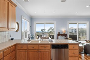 A modern kitchen with wooden cabinets, a stainless steel dishwasher, and a large window offering a view of the outdoors. - Blue Palms- 4/3 Gulf View home, WIFI, great views! (Cape San Blas)
