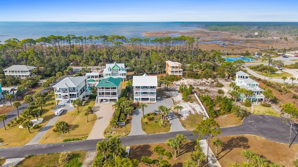 An aerial view of a coastal resort with multiple buildings, including a large resort building with a green roof, several smaller houses, and a beach area with a lifeguard tower. - Blue Palms- 4/3 Gulf View home, WIFI, great views! (Cape San Blas)