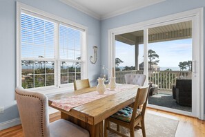 Un comedor con una mesa de madera, sillas y vista al océano a través de amplios ventanales.