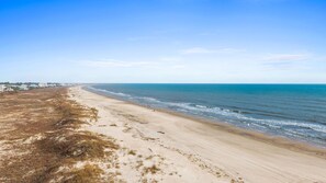 Una playa con cielo despejado, orilla de arena y algunos edificios a lo lejos.