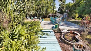 A wooden deck with chairs and a small table, surrounded by tropical plants and a sign reading "NYC". - 3B Near Englewood Beach! Pet Friendly Sunlit Home (Englewood)