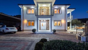 Uma casa de dois andares com varanda, entrada por meio de rampa e um jardim bem cuidado.