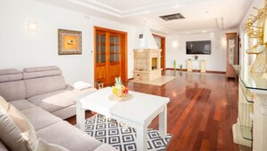 Uma sala de estar com sofá, mesa de centro com frutas, lareira e televisão na parede.