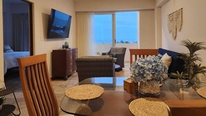 A modern living room with a glass table, wicker furniture, a TV mounted on the wall, and a view of the ocean through large windows. - Ocean View / Swimming pool / Wifi (Boca del Río)