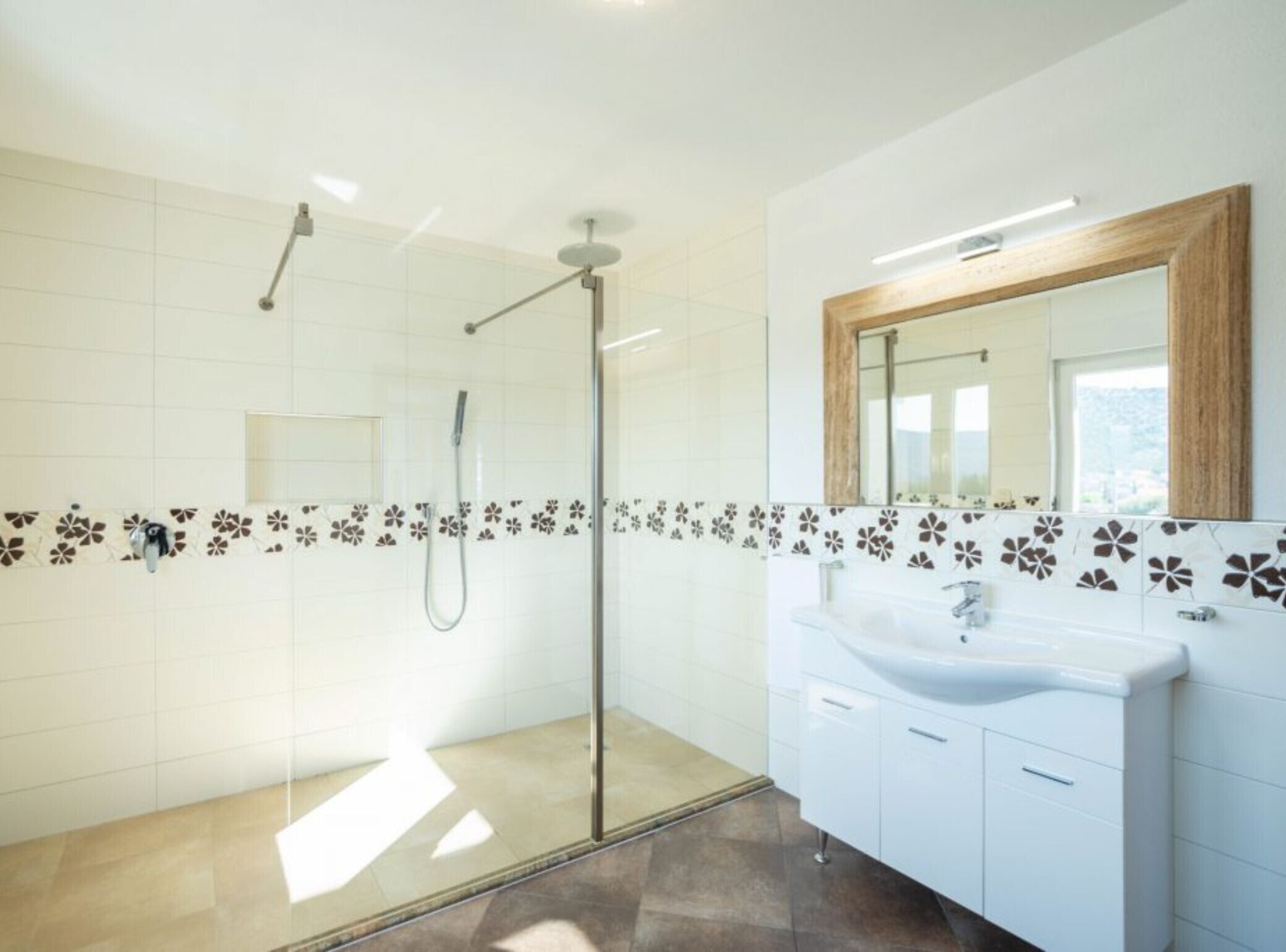 A modern bathroom with a glass shower enclosure, a white sink with a wooden mirror, and patterned tiles on the walls.