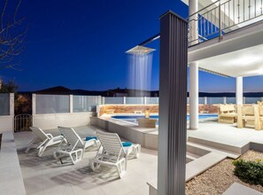 Eine Dachterrasse mit Whirlpool, Liegestühlen und einem Wasserfall.