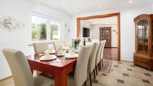 A dining area with a wooden table set for four, surrounded by chairs. There is a large wooden cabinet with glass doors to the right. - Guest House Matana Pomena National Park - Double Room-Diving (Pomena)
