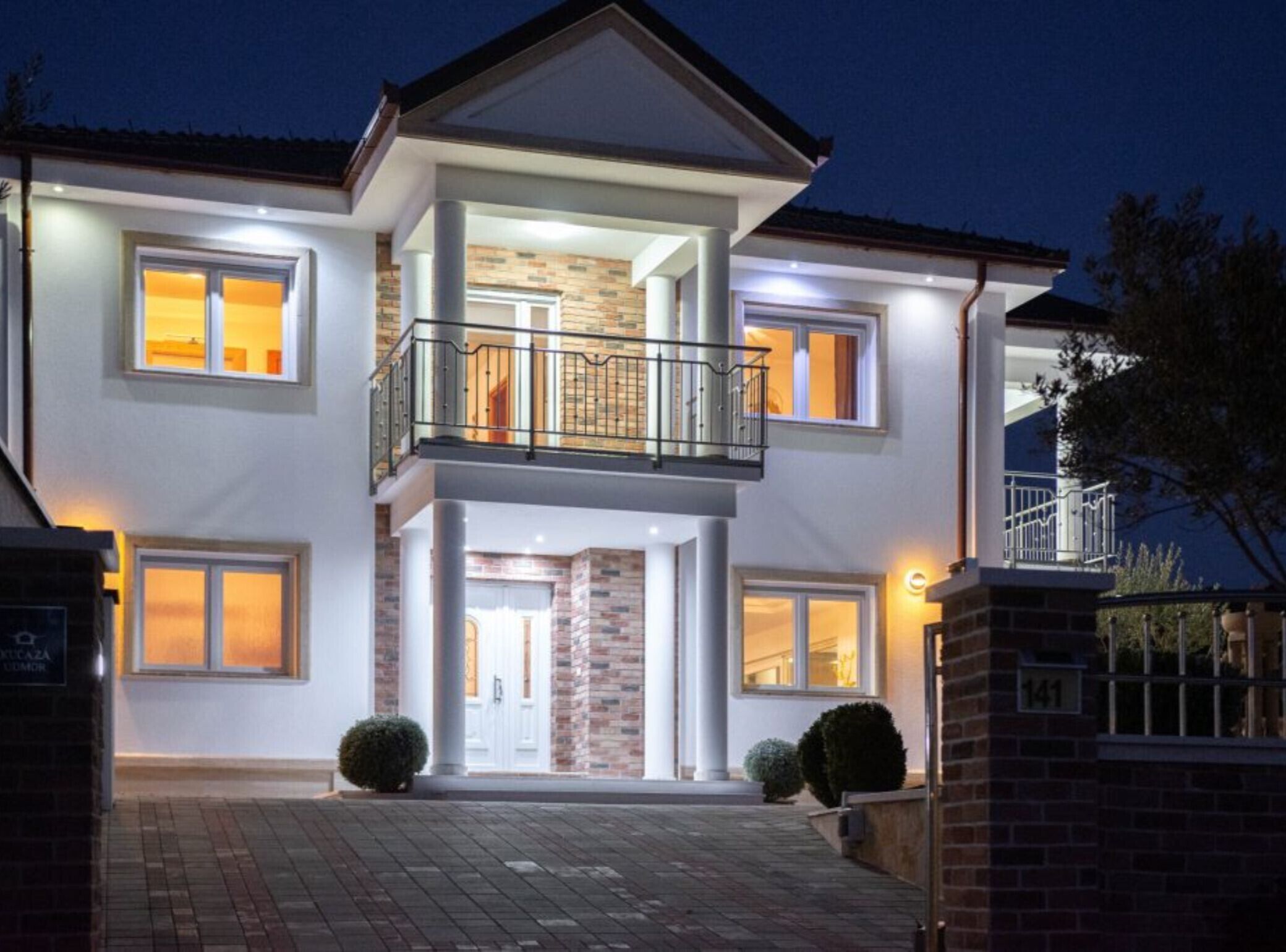 A modern two-story house with a balcony, large windows, and a brick facade.
