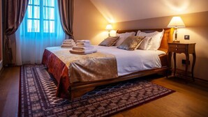 Una habitación de hotel con una cama grande, dos lámparas de noche, una mesita de madera y una alfombra estampada.