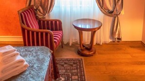 Hotellihuone, jossa on sänky, raidallinen nojatuoli, pieni pyöreä pöytä ja kuvioitu matto.